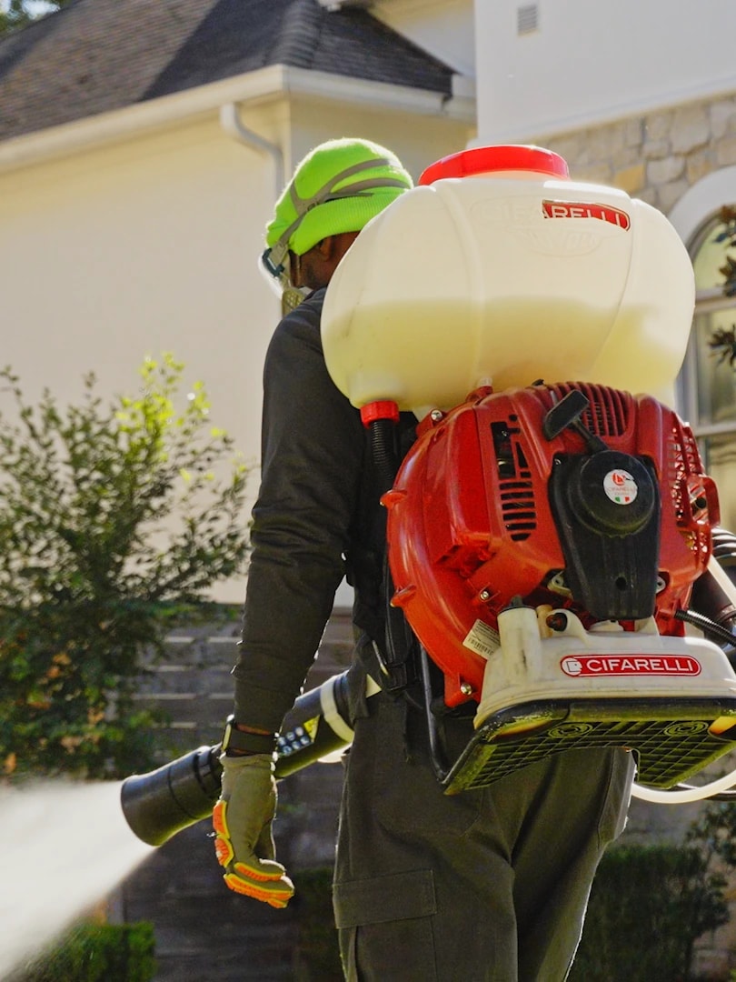 A technician treating the exterior of a San Antonio home with a backpack mist blower
