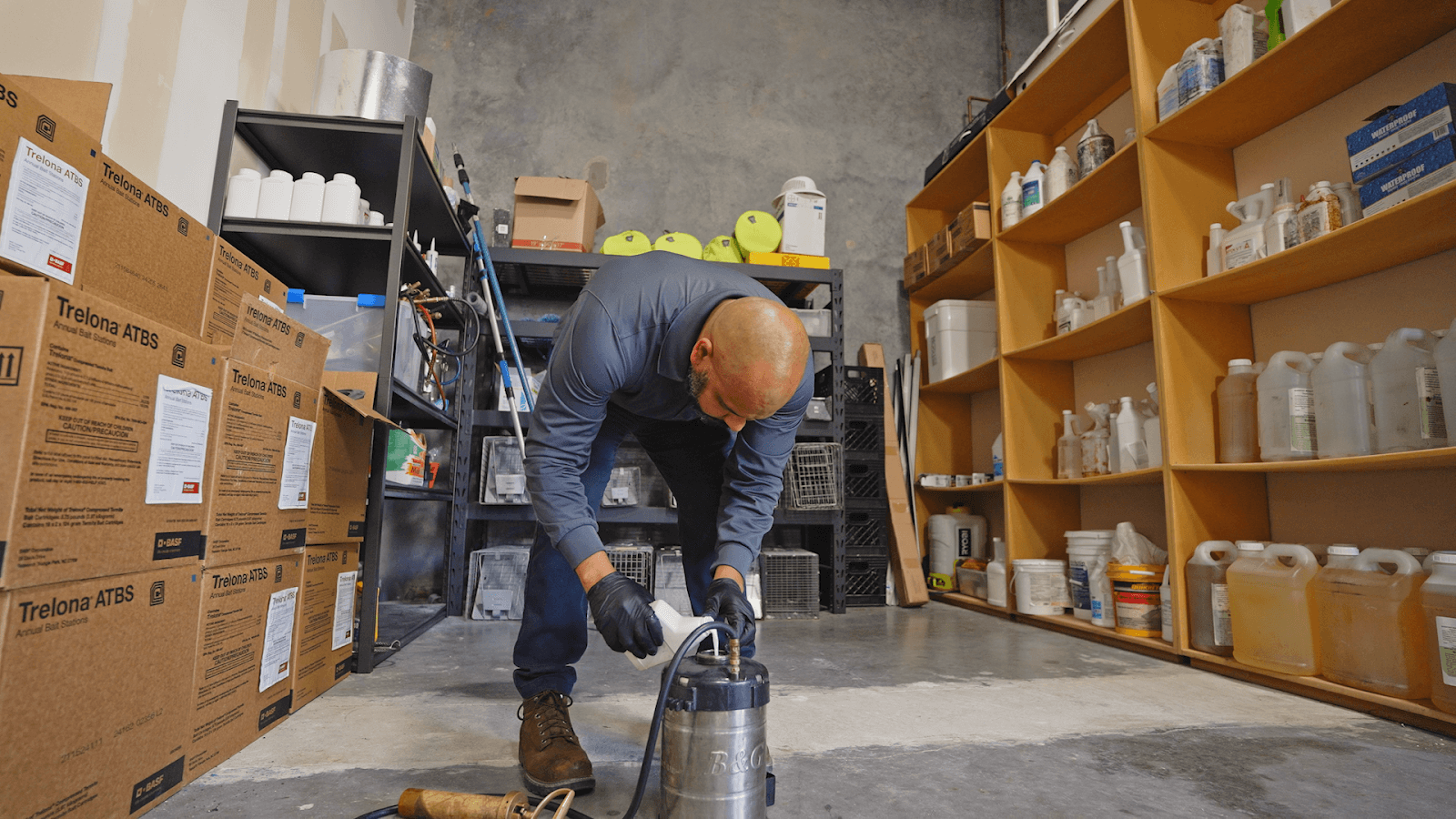 Technician wearing gloves pouring treatment mix into a stainless-steel pump sprayer in a supply room